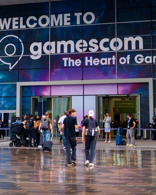 Entrance to the Gamescom 2026 exhibition hall with a "Welcome to Gamescom" banner and visitors walking toward the building.