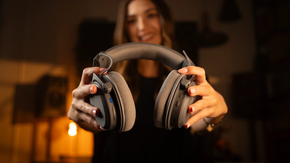 Close-up of a woman holding the ENDORFY Viro Infra Wireless Alt Gray headphones, highlighting the on-ear function buttons.