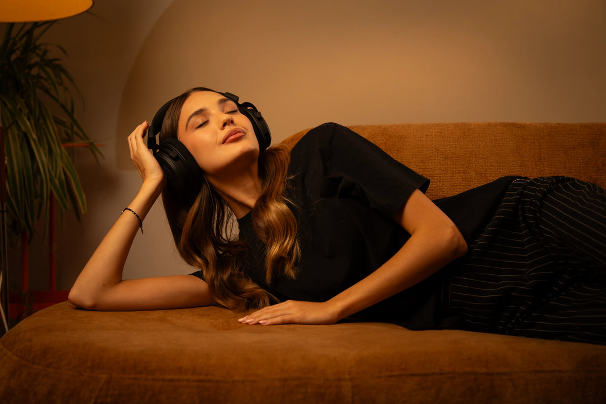 Woman relaxing in a semi-reclined position on the couch, eyes closed, enjoying music with the ENDORFY Viro Infra Wireless headphones